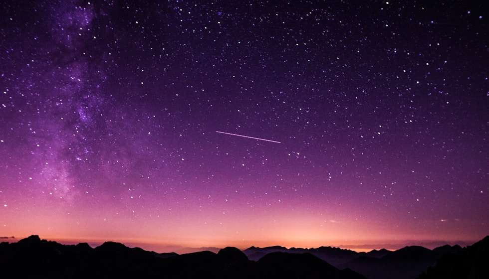 Purple starry night sky with shooting star over mountain silhouettes representing cosmic fortune and celestial guidance