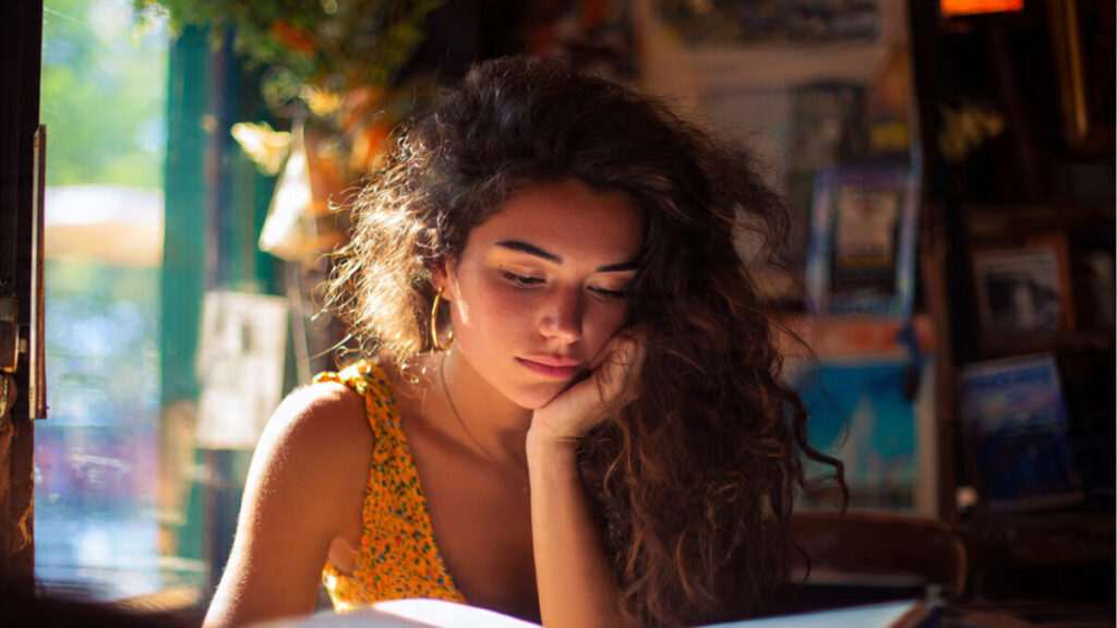 A thoughtful woman in a sunlit room, reflecting on her Mars and Venus love style as she reads.