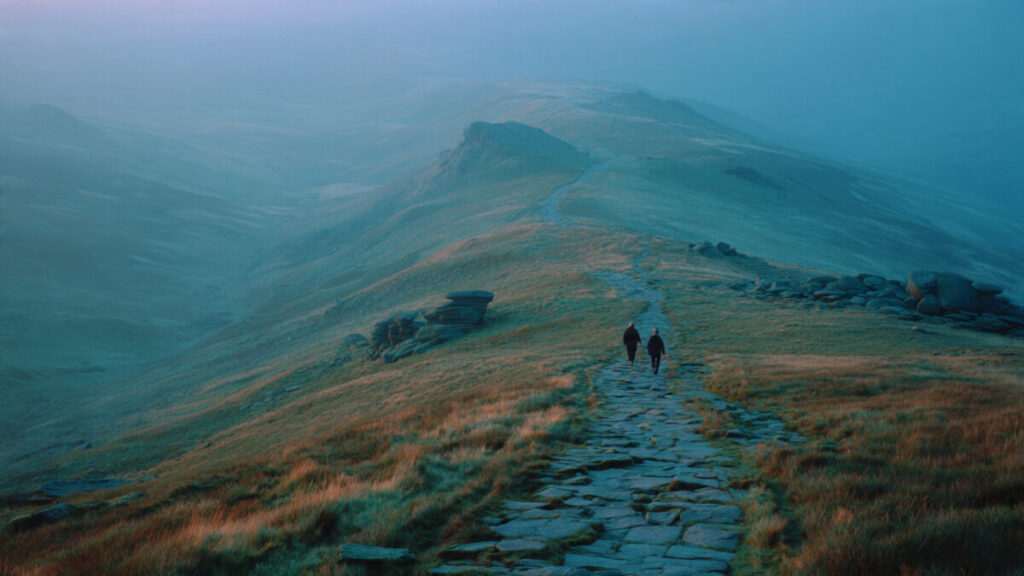 A wide, atmospheric landscape of misty green hills and a winding stone path, with two distant figures walking side-by-side into the fog.