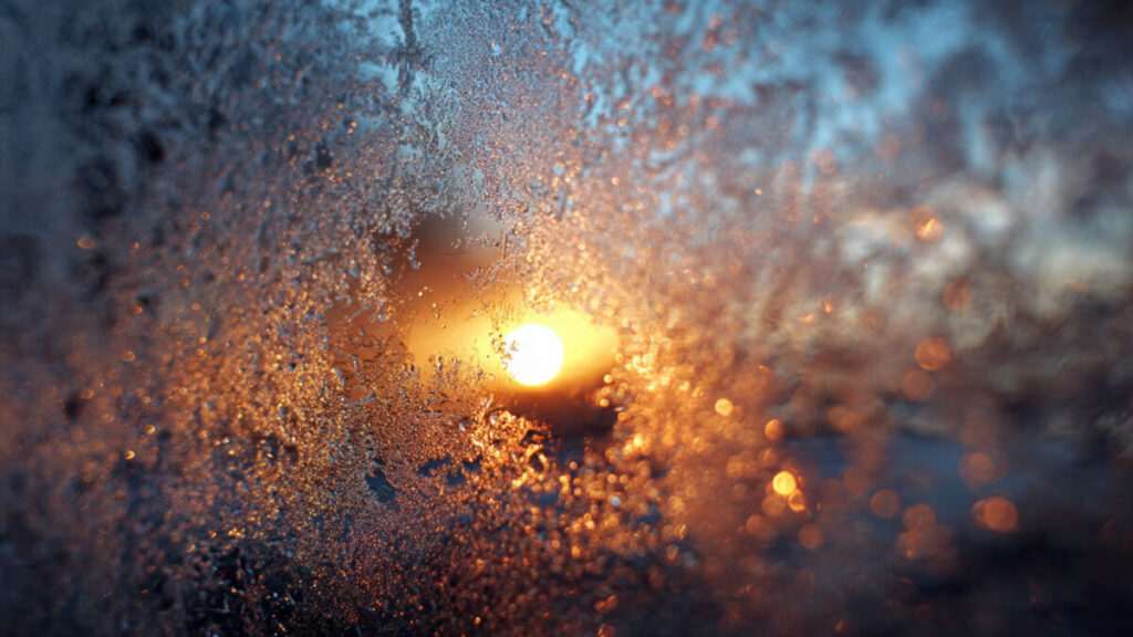 Frost melting on a windowpane revealing warm sunrise light, symbolizing heart chakra blockage release.